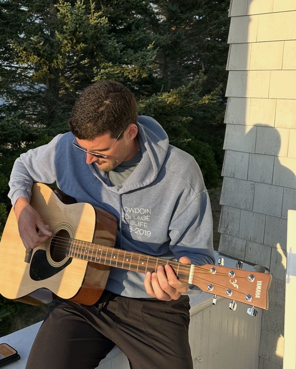 Collin van der Veen playing an acoustic guitar on a porch in Maine