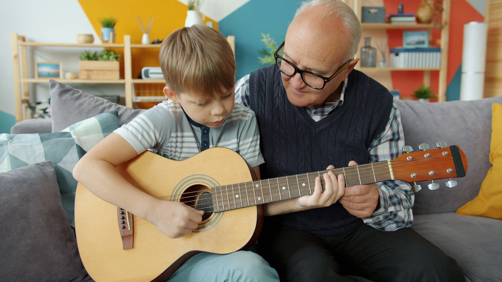 An older teacher shows a young boy how to hold a chord on an acoustic guitar